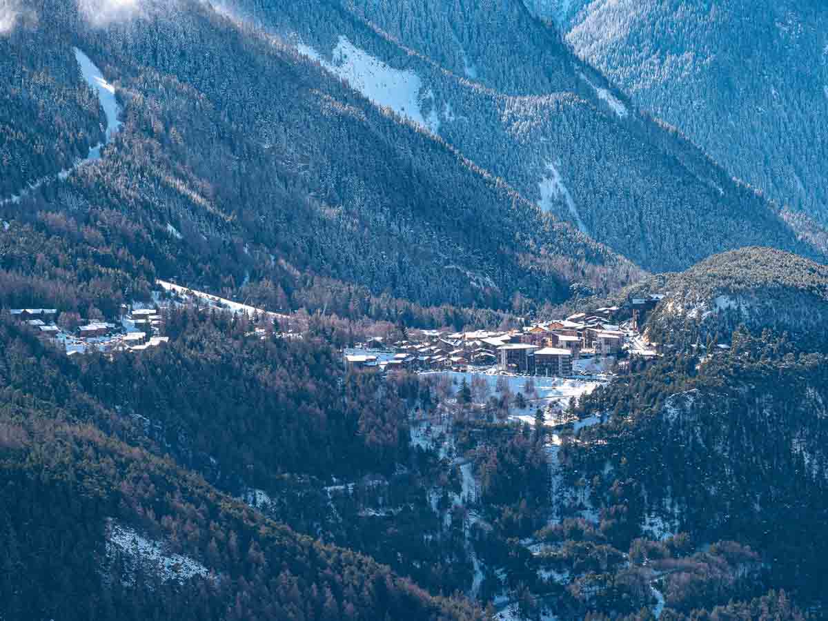 a far away shot of a high alpine village, surrounded by vast mountainous forest dusted in snow