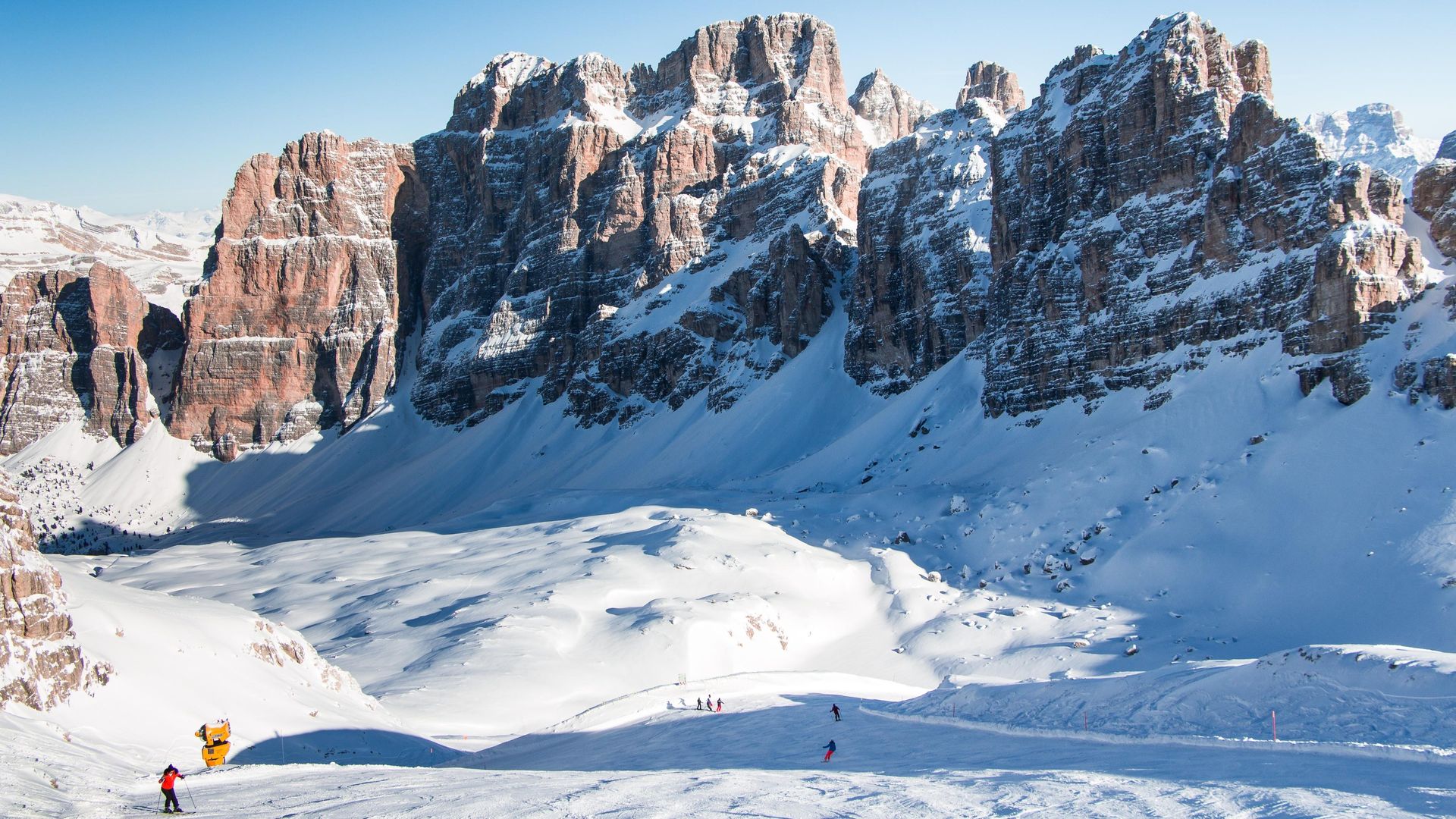 the sella ronda rock, and a piste beneath it, skiers tiny ants on the snow