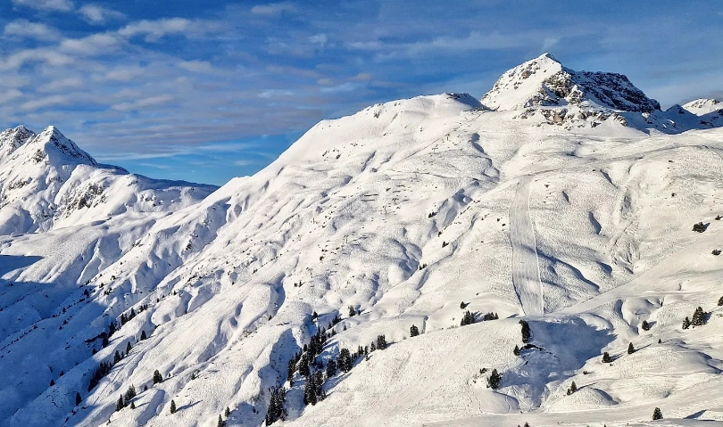 A pillowy haven of a ski mountain pictured from above/afar, with lift lines, ski pistes and ski tracks visible all over the mountain