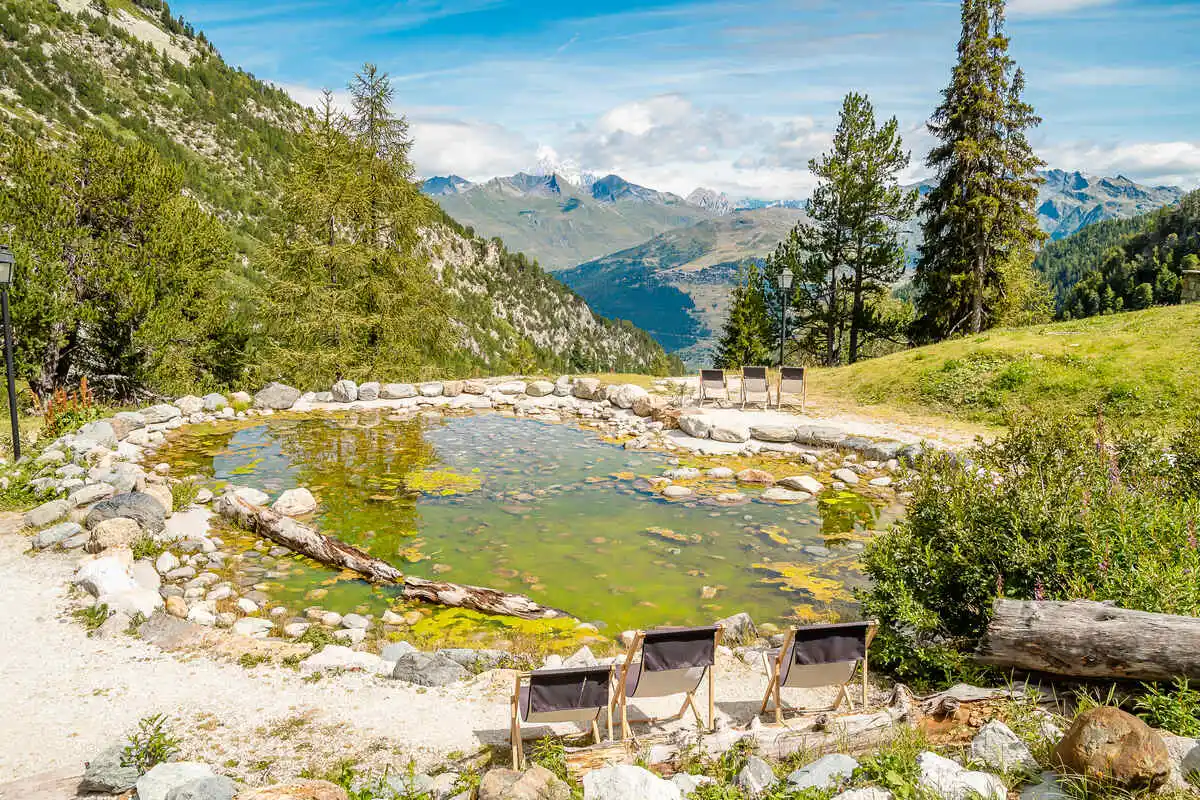 a shallow alpine lake with several deck chairs and huge views over mountain tops in summertime