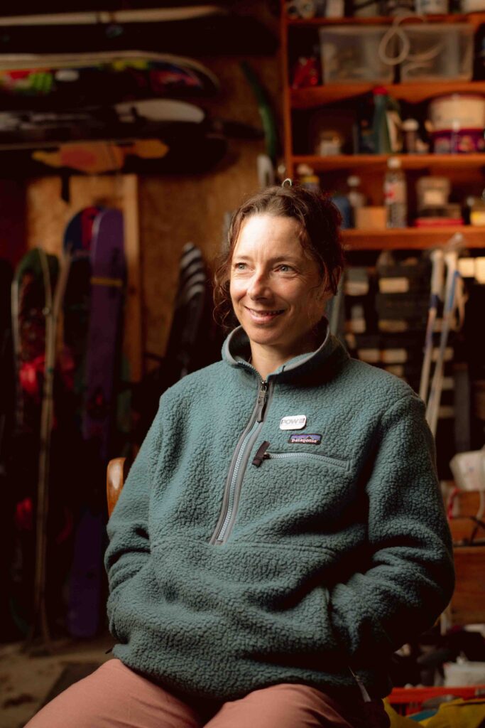 Snowboarder Lesley McKenna sits on a chair in a kit room, smiling beyond the camera