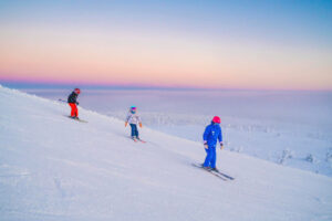 a pastel sky behind a ski instructor and two kids skiing what can only be Finland