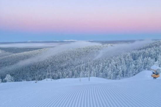 a pink sunset over a recently snowed-on ski area, with freshly groomed piste as the focus