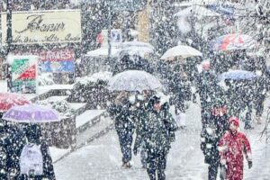 heavy snow falls as people walk the streets under umbrellas