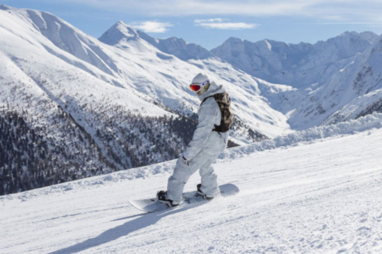 a snowboarder in white boards down a mellow bit of piste overlooking a white mountainscape