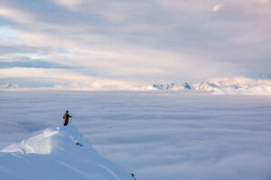 a skier standing on the edge of the world, above a sea of clouds
