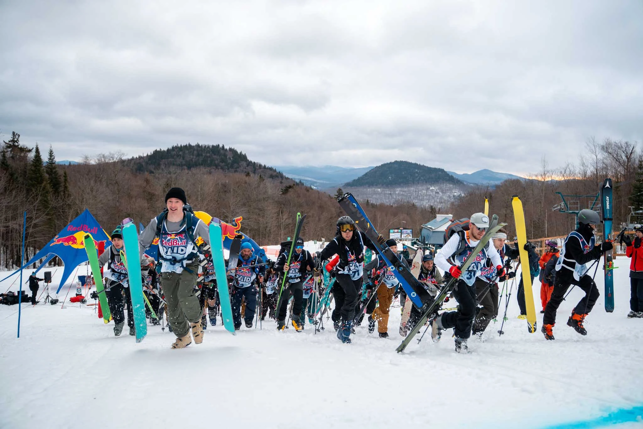 a Red Bull race start with dozens of skiers, skis with skins on in hand, running uphill