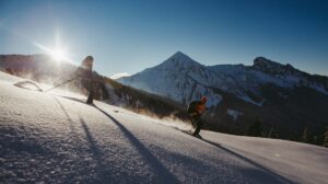 two skiers off piste in crystally glistening snow as sun crests over nearby hill