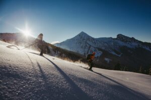 two skiers off piste in crystally glistening snow as sun crests over nearby hill
