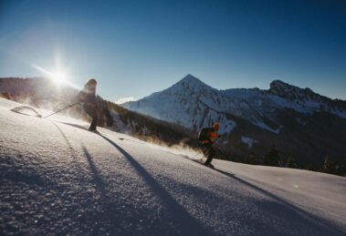 two skiers off piste in crystally glistening snow as sun crests over nearby hill