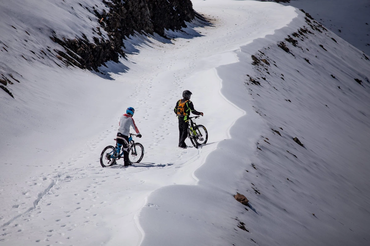 two mountain bikers look over the edge of a cat track covered in snow