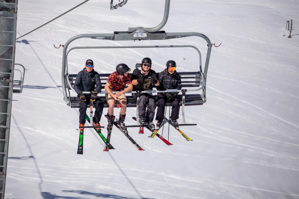 four skiers, with bare skin, sit on a chairlift for summer skiing