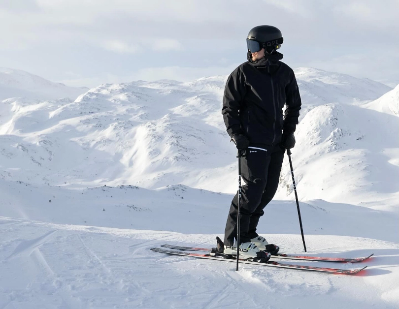 skier in black poses for camera, looking to the side on snowy plateau