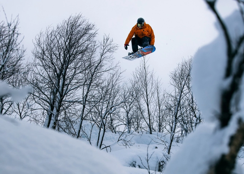 a snowboarder takes big air (or seemingly nothing) surrounded by bare trees