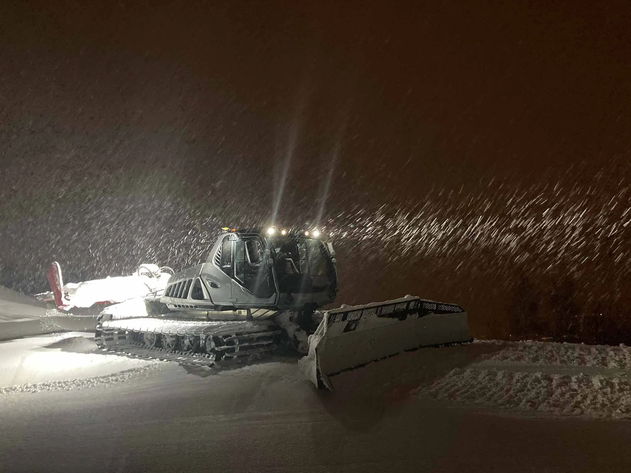 a piste basher at night, under light snow