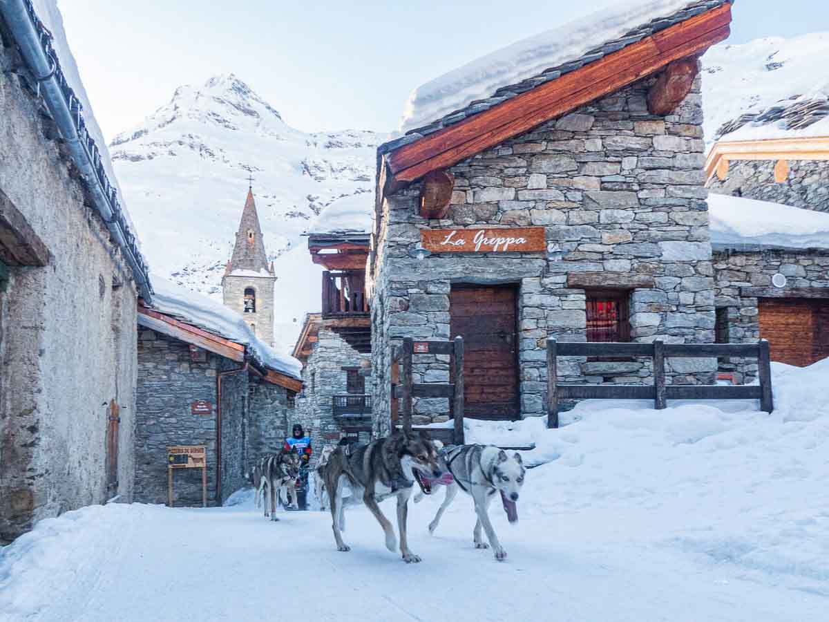 a husky sled runs through narrow snowy streets of old village Bonneval