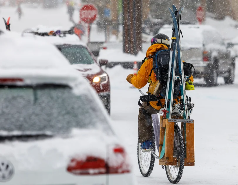 a biker with skis attached to bike, makes its way with the traffic in the snow