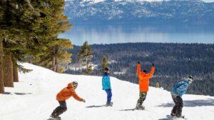 a crew of snowboarders, arms throw in the air, head away from the camera towards a snowless valley farther below