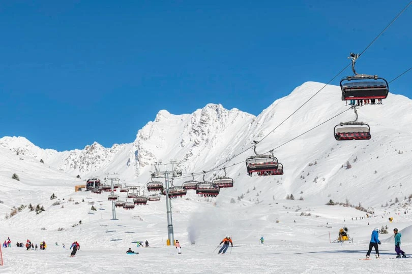 skiers on a wide open piste, under a chairlift, on a sunny day
