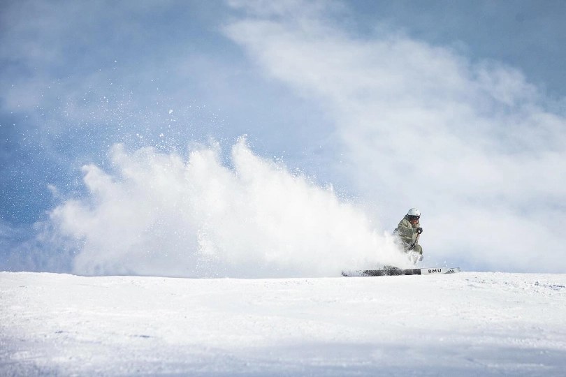 a skier brakes to spray dry light powder snow on the brow of a ski hill, blue sky behind