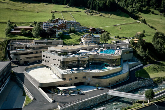 A huge spa-leisure centre complex is pictured, super modern, built in to the mountain, with outdoor pools visible on various layers of building