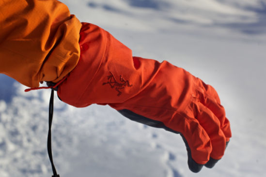 orange gloved hand and lower arm held out against the snow