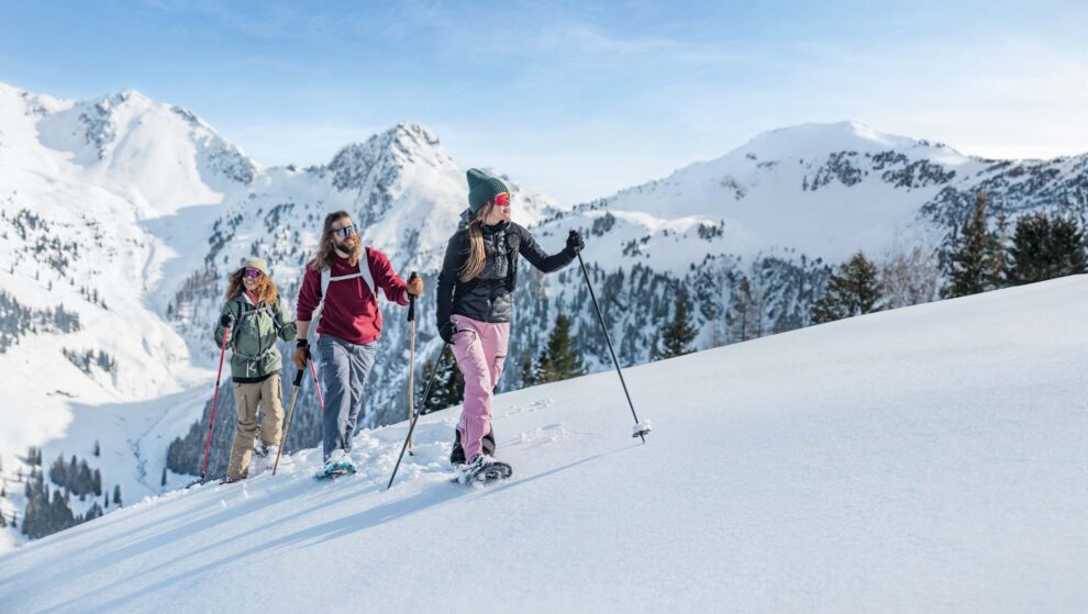 Snowshoeing trio look happy and around them on the uphill on fresh snow in Austria