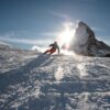 a skier skis towards the camera, resting on the snow, with the Matterhorn behind as the sun goes behind the mountain