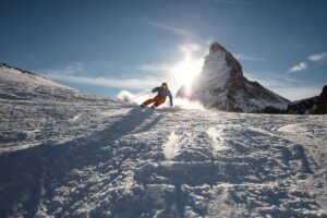 a skier skis towards the camera, resting on the snow, with the Matterhorn behind as the sun goes behind the mountain