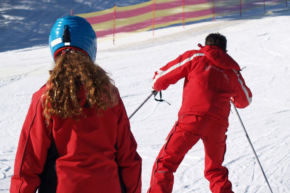 Young girl follows a ski instructor in red uniform during a lesson