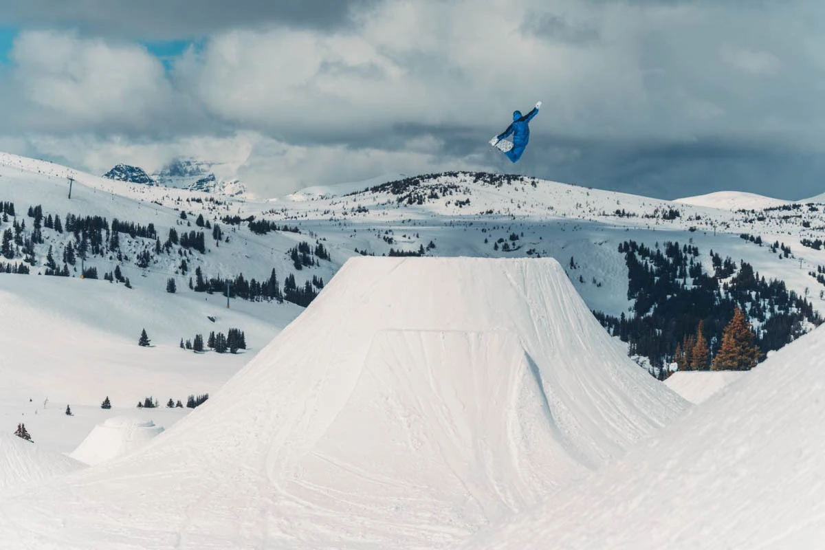 a snowboarder in blue takes off a huge kicker in the snowpark of a ski area
