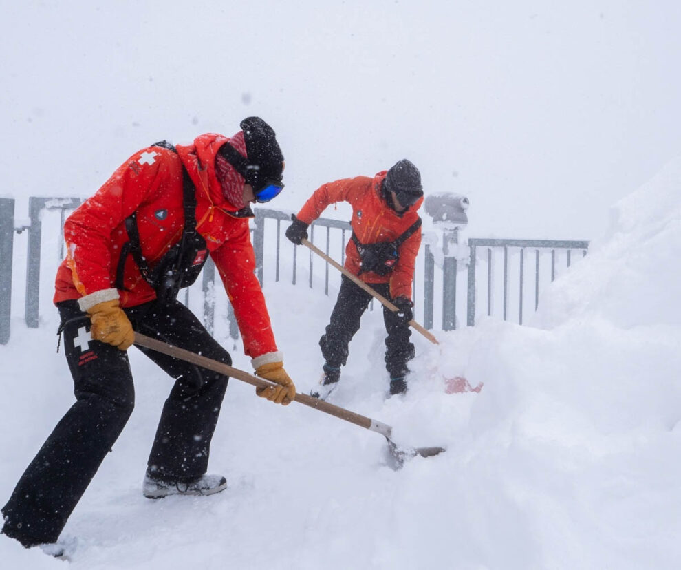 patrol guys digging fresh fallen snow in a whiteout
