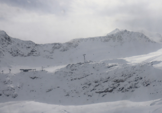 A hazy light with light clouding covers two high mountain ridges covered in snow in the Pitztal ski area
