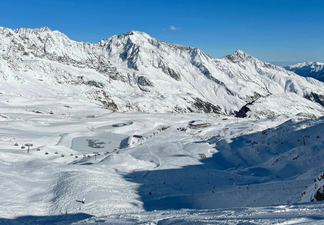A mega shot of a snowy ski area, with lifts, pistes and peaks included under a blue sky