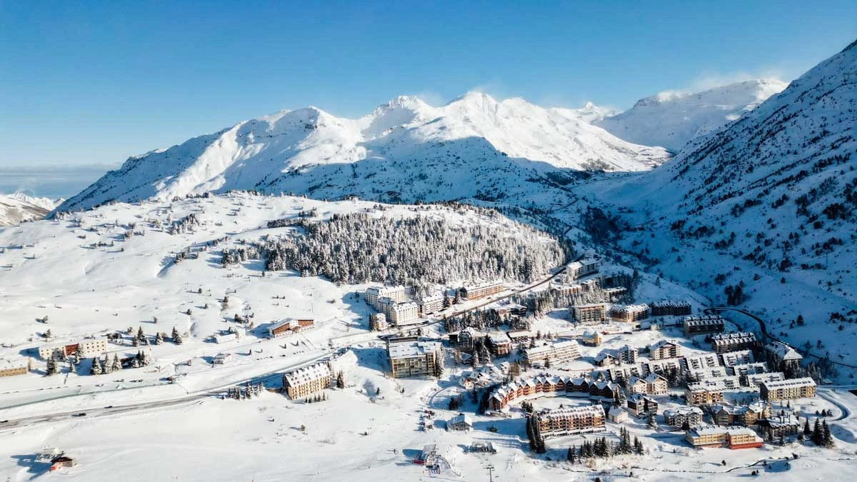 a small ski village is photographed from above with snowy roofs, surrounded by snow fields and peaks