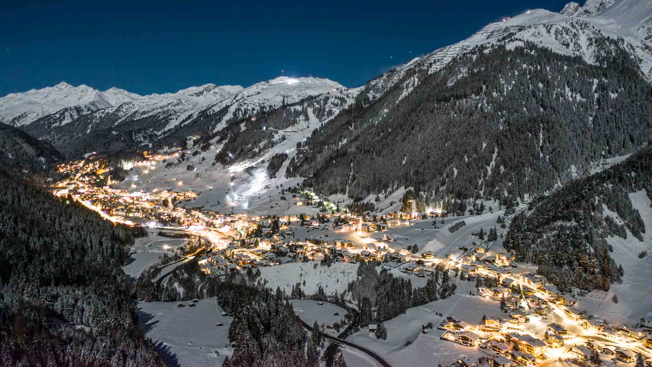 St Anton shot from above, lit up at night, sprawling across the valley floor