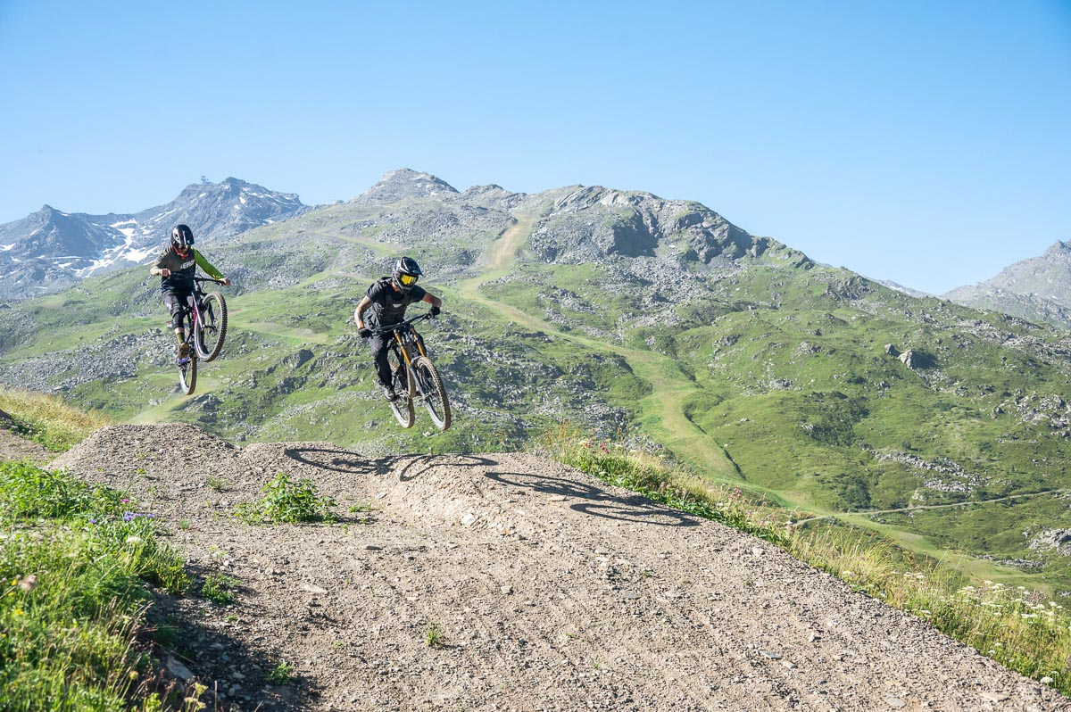 two mountain bikers take air off small terrain jump high in sunny mountains