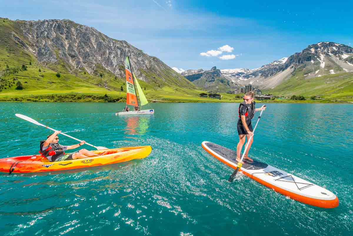 SUPs and a windsurf on a blue lake surrounded by green mountains