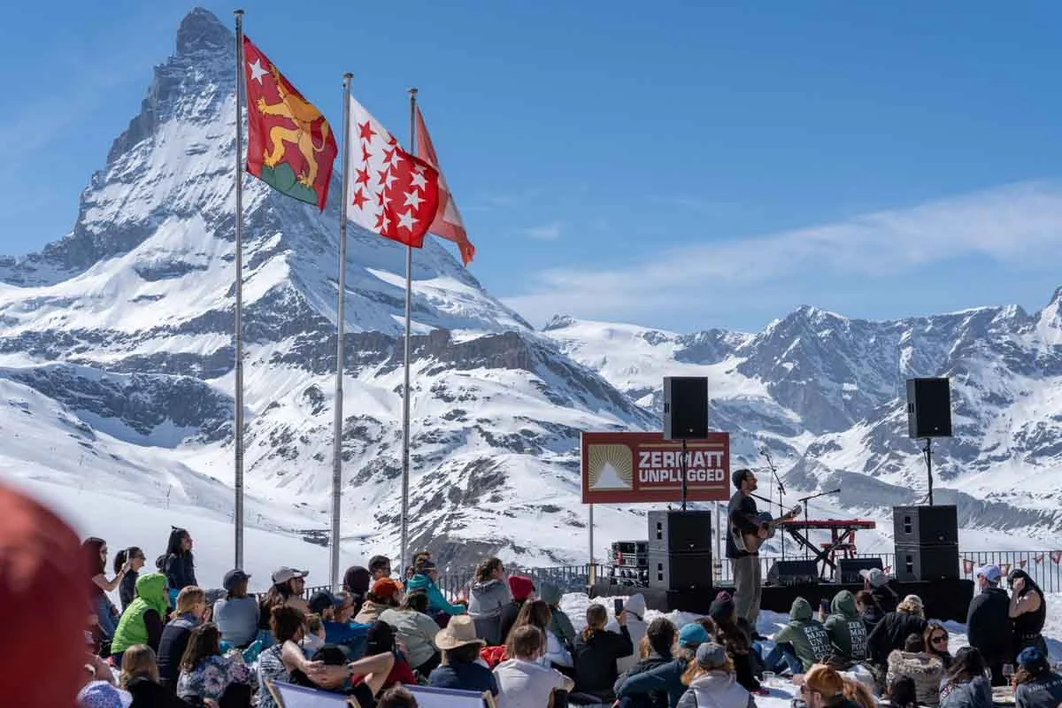 a deck full of people watching a musician perform, the matterhorn the backdrop