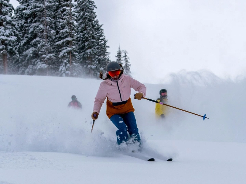 three skiers smile large, skiing towards camera through fresh light snow