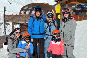 grandparents, parents and young kids pose for ski photo outside a chalet on the snow