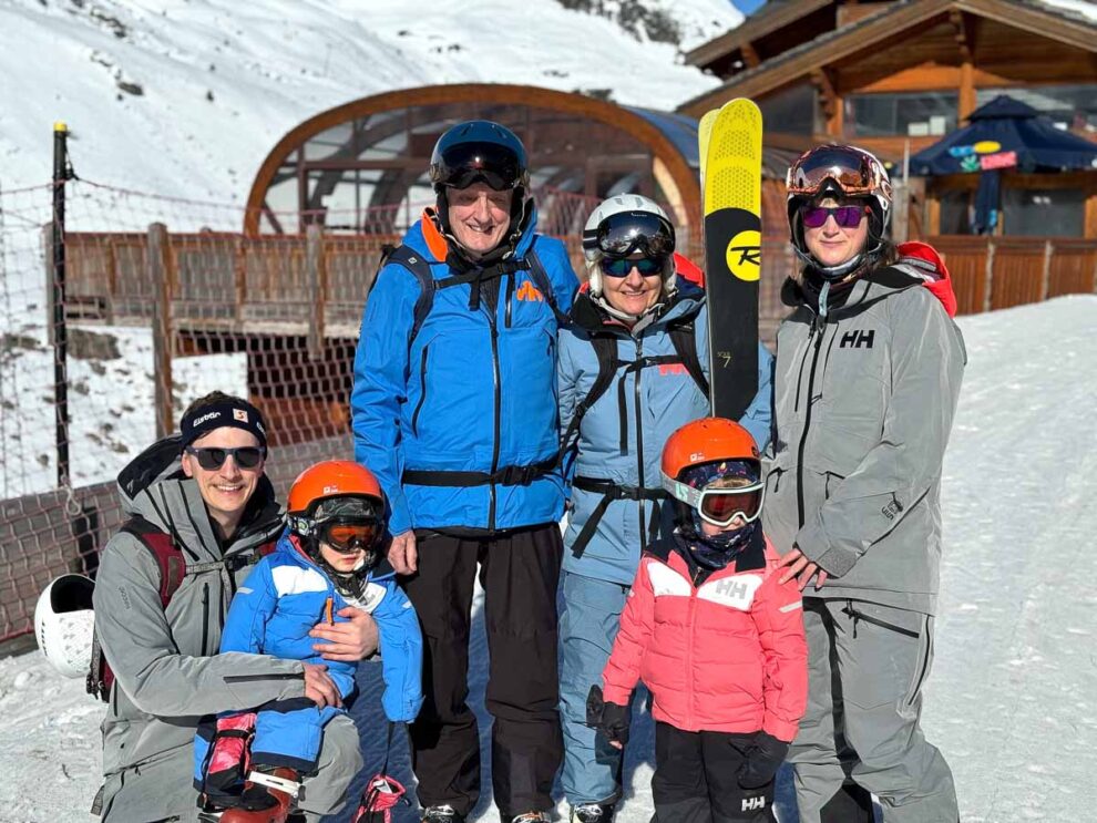 grandparents, parents and young kids pose for ski photo outside a chalet on the snow