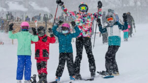 family skiing with three kids, poles and arms in the air
