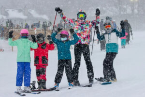 family skiing with three kids, poles and arms in the air