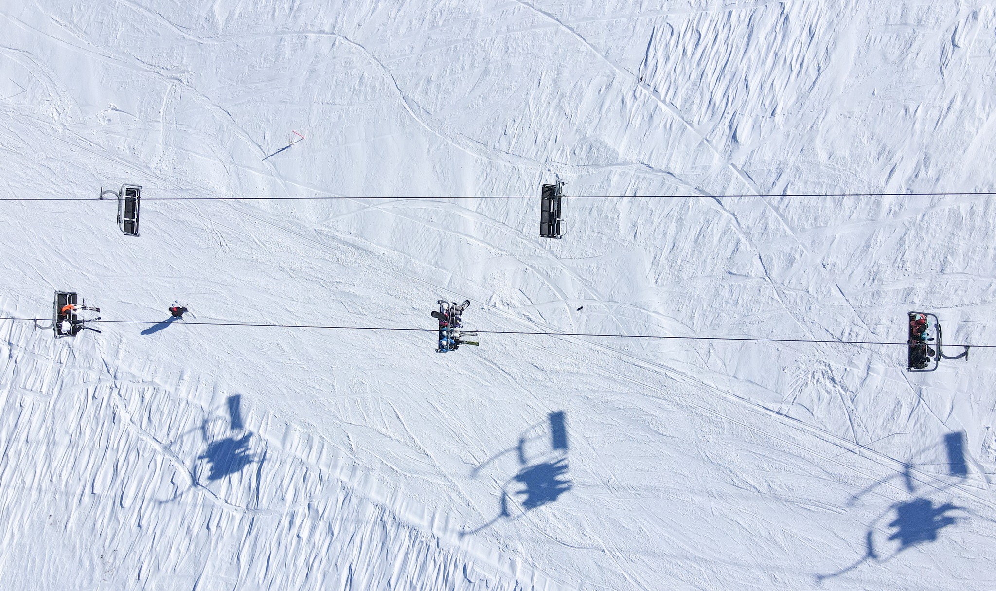 aerial shot of a chairlift over slope, the shadows of moving chairs reflected on white snow
