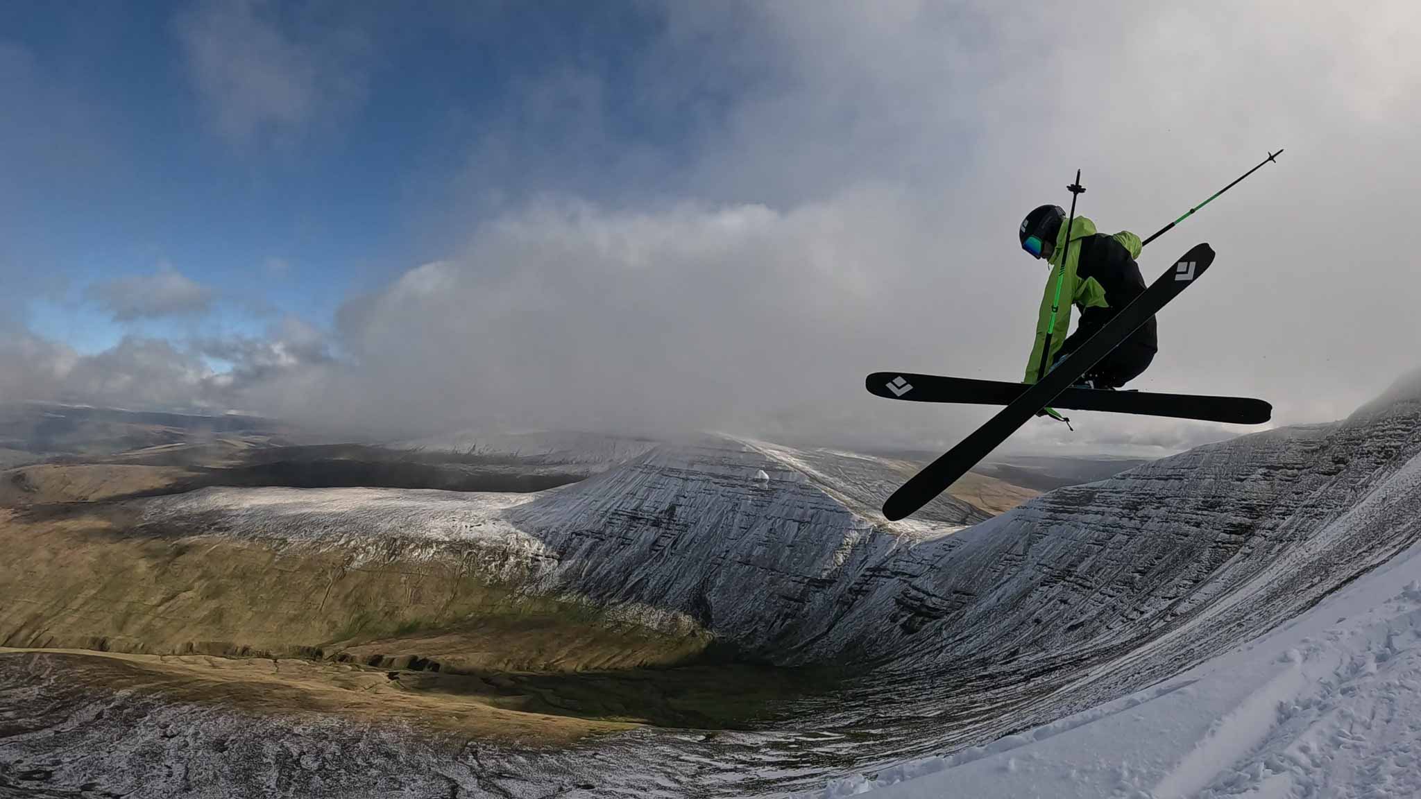 skier grabs skis in air, over barely covered snowy slopes in what can only be Wales