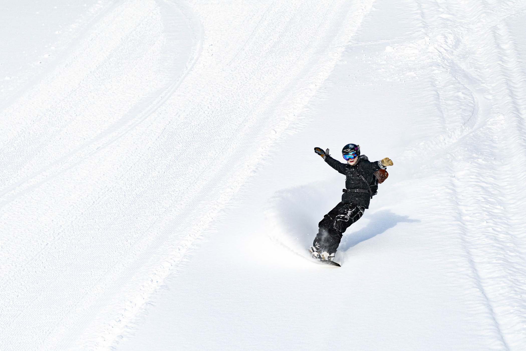 a snowboarder, snow in beard, opens arms as he descends fresh powder next. to the piste