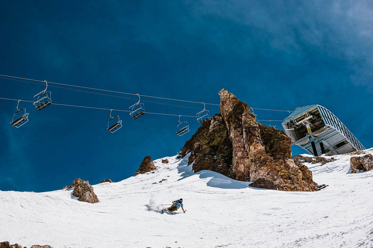 a skier skis off piste under a chairlift on a blue sky day