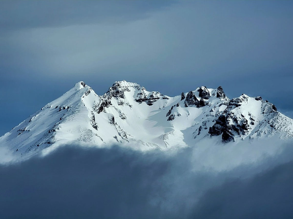 a cloud covers the bottom half of a mountain massif, covered deep in snow