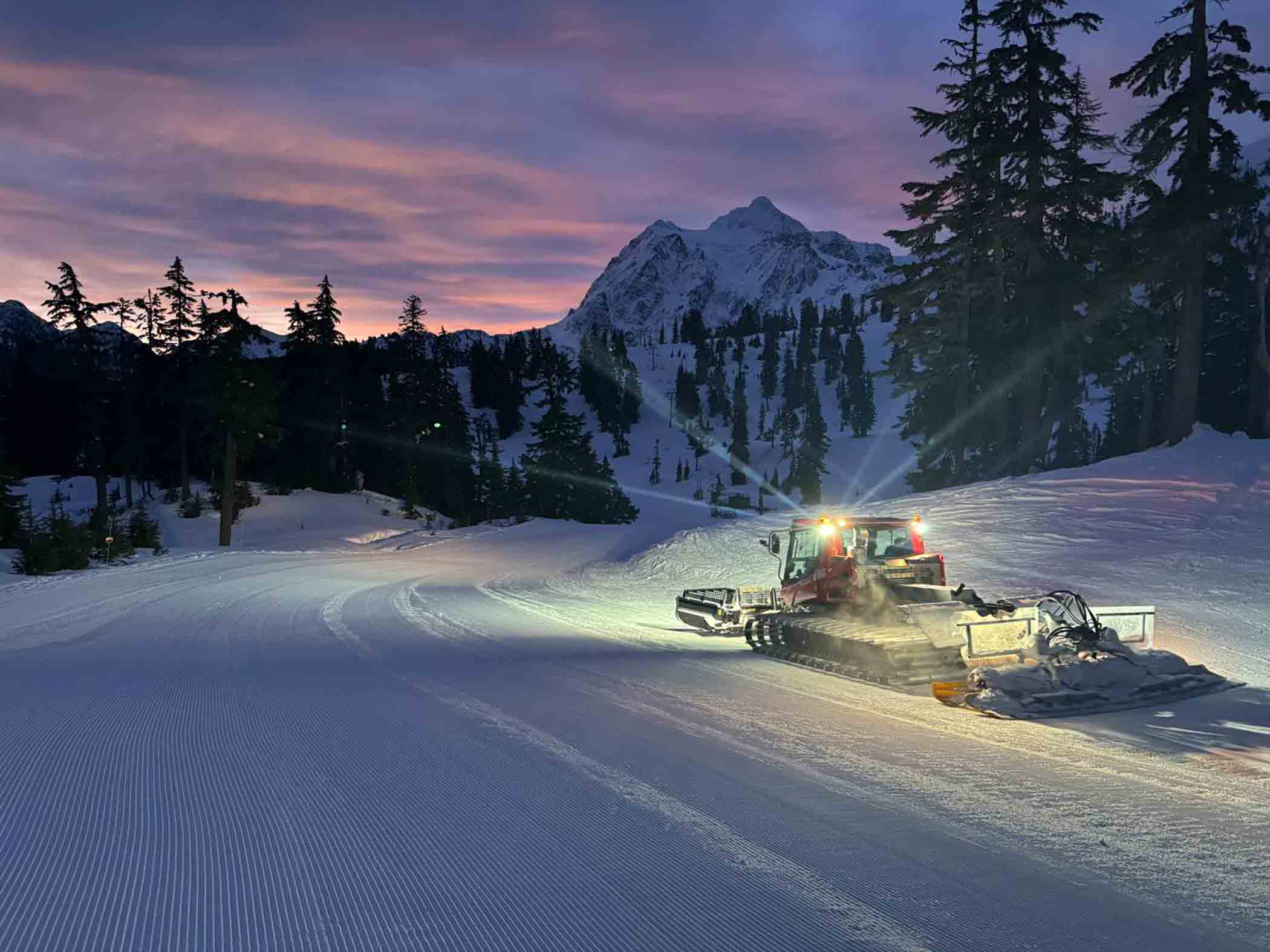 a snowcat sets out to work under a pink sky in the snowy mountains
